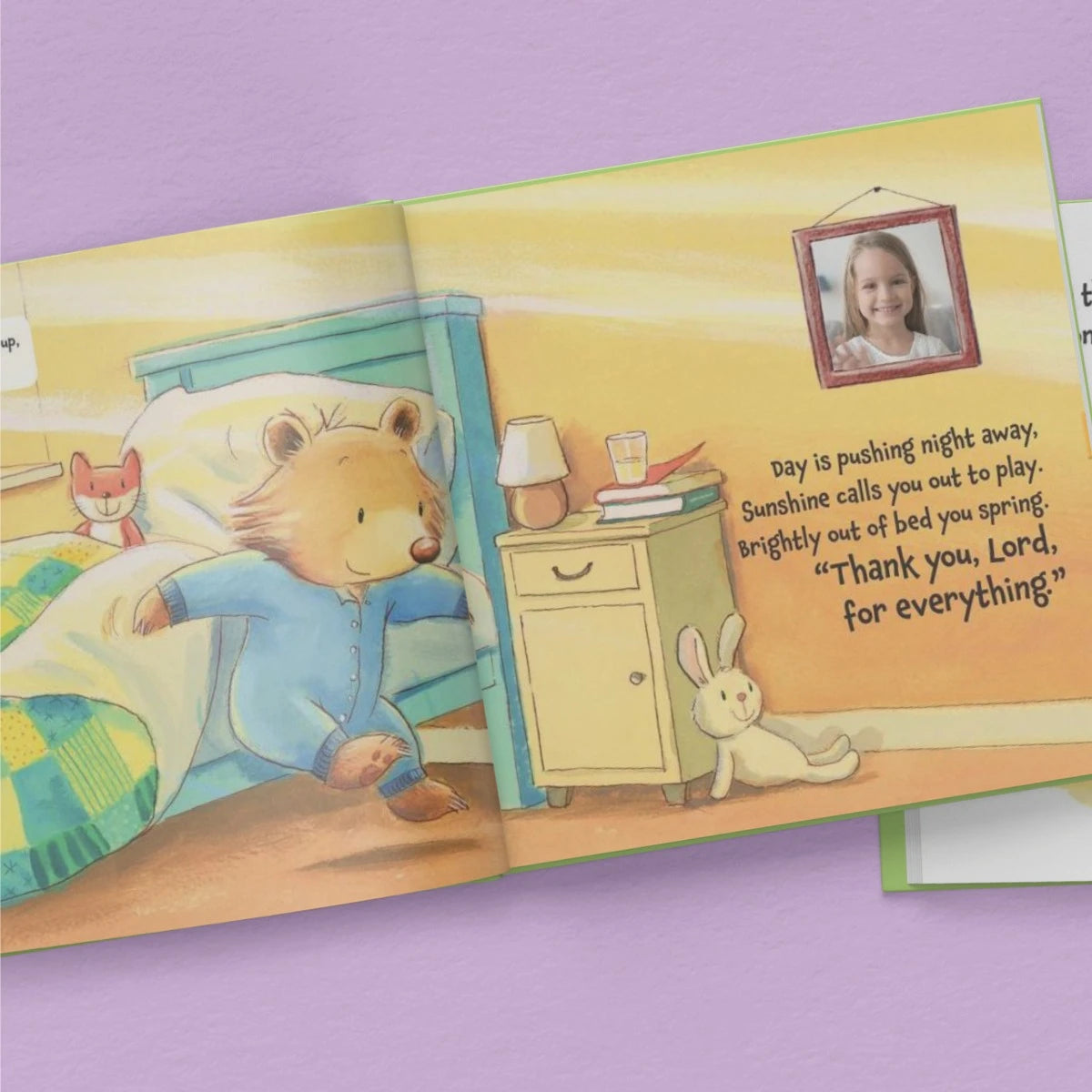Illustrated children's book open to a page with a bear character and a photo of a girl on a purple background