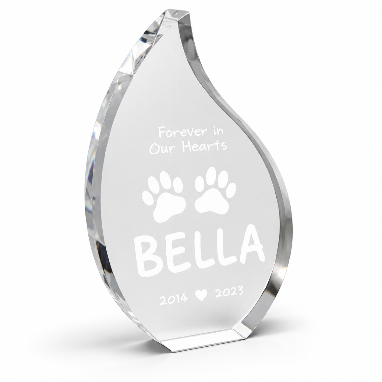 A clear acrylic or glass teardrop-shaped memorial award plaque engraved with the text 'Forever in Our Hearts', two paw prints, the name 'BELLA', and the years '2014' and '2023'.