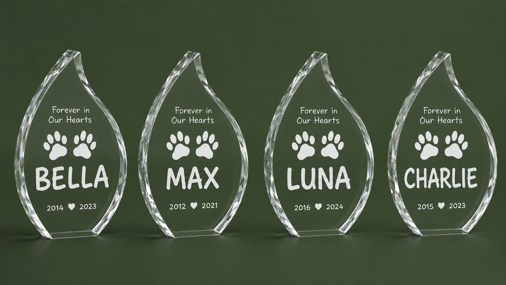 Four clear acrylic pet memorial award plaques on a dark green background, each shaped like a teardrop with engraved paw prints and a pet name: BELLA, MAX, LUNA, and CHARLIE.